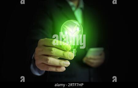 A hand of a businessman holding light bulb with leafs and light. The idea concept with innovation and inspiration for an environmentally friendly or g Stock Photo