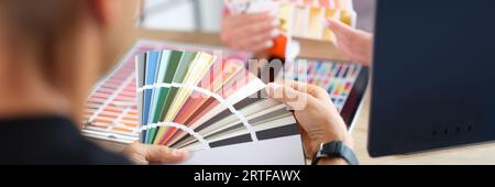 Manager and client holding color swatch cards while sitting at table in design studio. Stock Photo