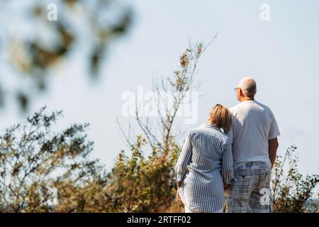 Happy elderly couple hold hands, communicate, look at the sea. The woman leaned her head on the man's shoulder. Enjoy sea views. Stock Photo