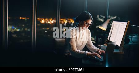 Caucasian businesswoman working late at night in her office, typing on her laptop to meet a project deadline. She is focused, determined and committed Stock Photo