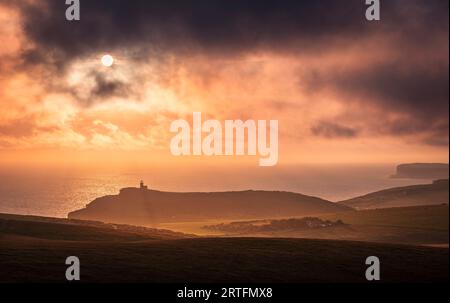 Dramatic skies and sunset behind Belle Tout lighthouse from the cliff edge of Beachy Head on the south downs east Sussex coast south east England UK Stock Photo