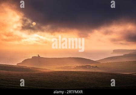 Dramatic skies and sunset behind Belle Tout lighthouse from the cliff edge of Beachy Head on the south downs east Sussex coast south east England UK Stock Photo