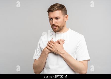 Man has breathing problems, panic attack, suffocation holding hands on chest on gray background. Stock Photo