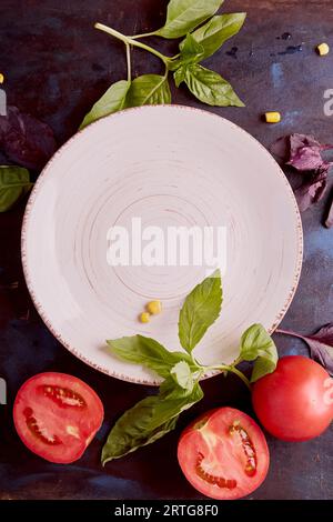 Empty white plate mockup in the center among organic vegetables and greens. Keto, FODMAP, Paleo, Plant-based diet concept top view. Stock Photo