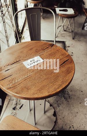 Chairs and wooden table with sign No Laptops. No wi-fi zone in urban cafe. Breakfast table. Modern lifestyle. Sign with words No laptops. Stock Photo