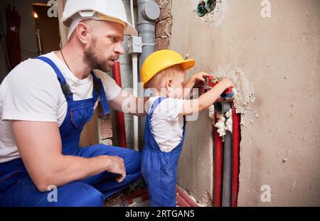 Father and son using spirit level tool while installing plumbing pipes in apartment. Male plumber and child measuring pipes level with building instrument. Stock Photo