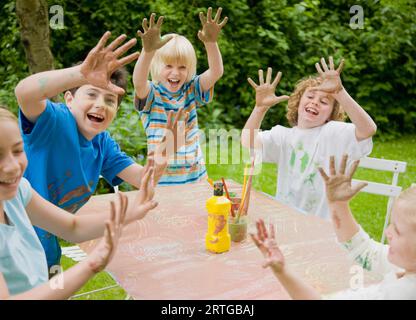 Children smiling and laughing with their arms up and hands covered in paint Stock Photo