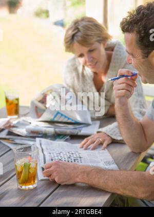 Couple sitting outside drinking cocktails and doing crossword Stock Photo