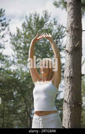 Young woman doing yoga standing in a forest in the raised hands pose Stock Photo