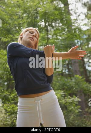 Young woman standing in a forest stretching her arm Stock Photo