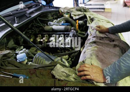 mechanic hands rests on an edge of motor compartment with combustion engine of german SUV with removed valve cover and rocker arms shaft during repair Stock Photo