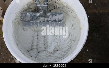 a shaped spatula in a plastic bucket with a viscous, viscous elastic solution as a plasterer's set for finishing, stirring the putty in the container Stock Photo