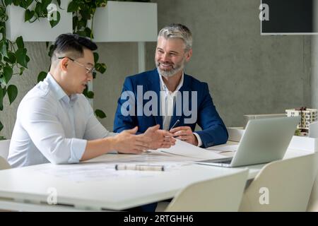 Men architects working on construction plans, engineers discussing on project in office. Stock Photo