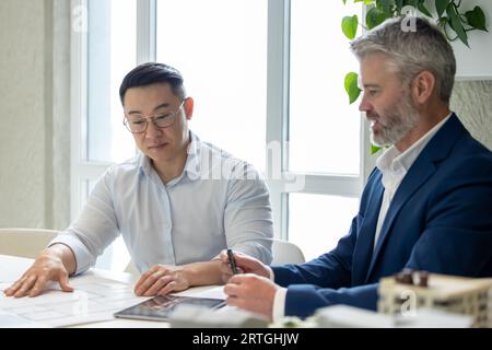 Men architects working on construction plans, engineers discussing on project in office. Stock Photo