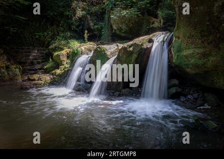Falling water and an enchanting waterfall named 'Schiessentumpel' between the solid rocks in the forest of Mullerthal, a fairytale setting in Luxembou Stock Photo