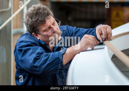 A builder of wooden boats scribing trim to accurately measure a trim piece to fit to a hull Stock Photo