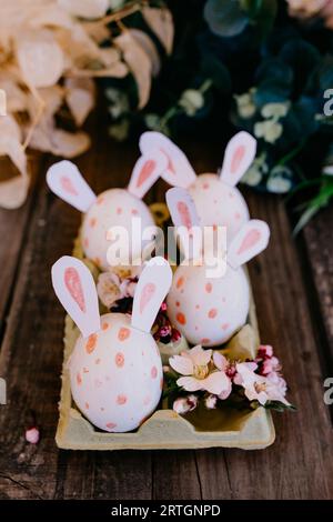 Closeup set of colored chicken eggs with decorative rabbit ears in container on wooden background Stock Photo