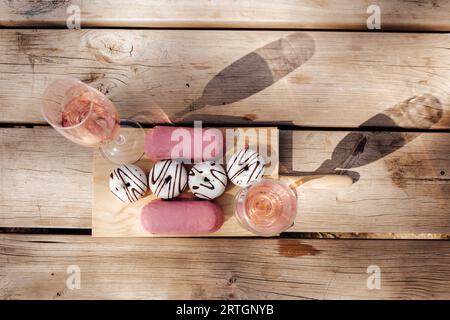 Glasses with fine pink wine placed on wooden surface near set of fresh delicious doughnuts Stock Photo