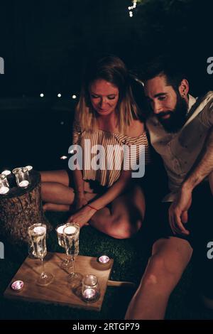 Young man and woman sitting on lawn near glowing candles during night in dark night garden Stock Photo