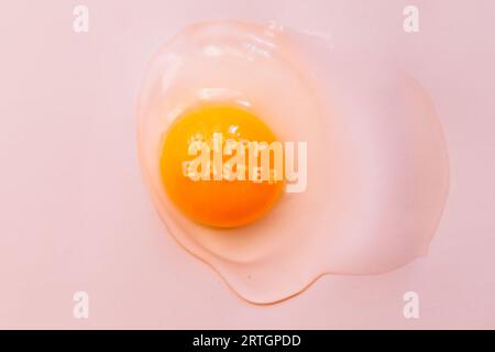 From above raw broken egg with text Happy Easter on yellow yolk on pink background Stock Photo