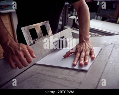 From above anonymous man using wooden workbench with paper sheets and measuring detail while standing near table Stock Photo