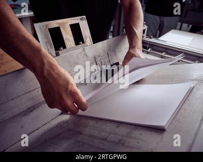 Unrecognizable man working with papers while standing at table and checking paper sheets in workshop Stock Photo