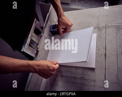 From above of crop unrecognizable male artisan putting paper sheets in stack on table while working in professional workshop Stock Photo