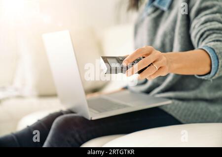 Crop unrecognizable female remote worker sitting on sofa and using remote control while working on netbook at home Stock Photo
