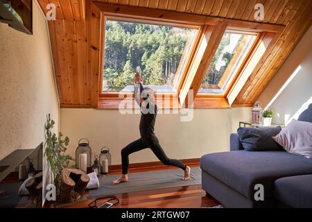 Side view full body of slim boy in sportswear standing in pose while doing yoga on mat in living room with couch Stock Photo