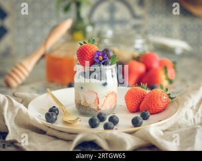 Healthy yogurt with fresh strawberries and blueberries in glass jar placed on plate with spoon on table for breakfast Stock Photo