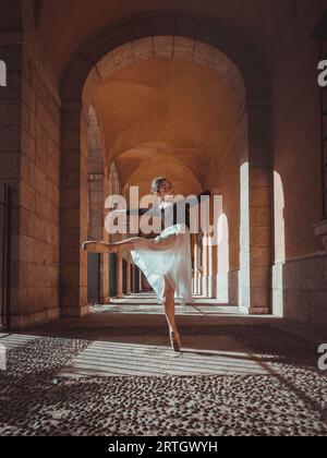 Side view of full body of young gracious female ballet dancer performing arabesque position in arched corridor Stock Photo