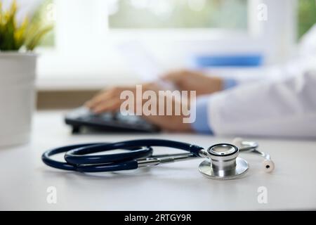 stethoscope on the table in clinic office. doctor working on computer in background Stock Photo