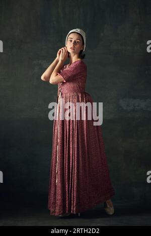 Portrait of elegant woman in image of medieval maid, wearing vintage costume against dark vintage background Stock Photo