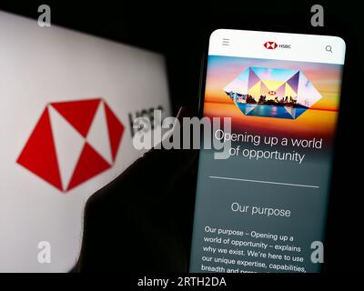 Person holding smartphone with website of financial services company HSBC Holdings plc on screen with logo. Focus on center of phone display. Stock Photo