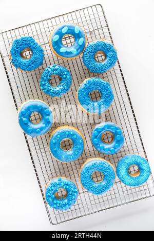 A cooling rack topped with homemade blue melted chocolate candy decorated donuts Stock Photo