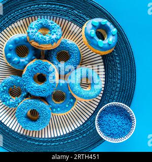 A pile of blue chocolate dipped decorated donuts with a bowl of sprinkles. Stock Photo