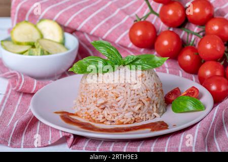 Dish with tomato rice dome, red cherry tomatoes, basil leaves and courgettes cut into wheels Stock Photo