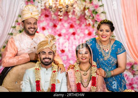 Portrait of Happy smiling Indian middle aged Father and Mother with newly wed daughter and son in law posing to camera on wedding stage - concept of Stock Photo