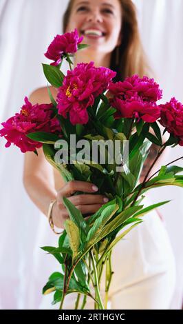 happy woman holding peony bouquet in front of face in the morning, sweet romantic moment Stock Photo
