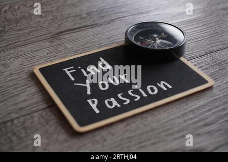 Closeup image of compass and chalkboard with text FIND YOUR PASSION on table. Stock Photo