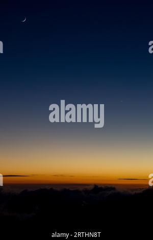 Crescent moon above the horizon illuminated by the sunset at Mauna Kea on Big Island, Hawaii, USA Stock Photo