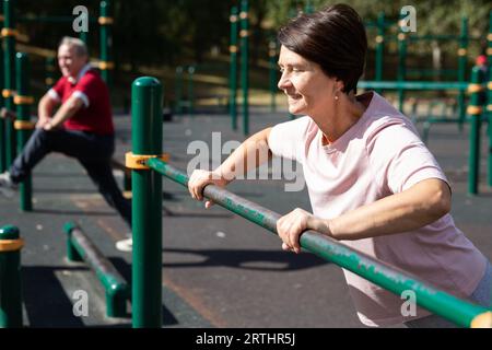 Mature woman doing push-ups from the crossbar on outdoor sports ground Stock Photo