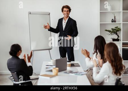 Happy male business trainer or team leader standing near whiteboard making presentation at meeting for colleagues Stock Photo