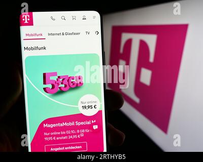 Person holding mobile phone with web page of telecommunications company Deutsche Telekom AG on screen with logo. Focus on center of phone display. Stock Photo