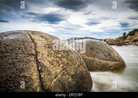 Close-up of the Moeraki Boulders round rock formations in Moeraki, New Zealand. The long-exposure captures the movement of clouds and waves around Stock Photo