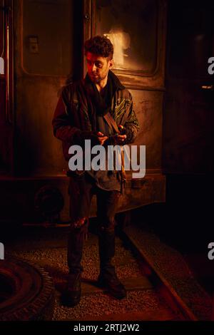 man in dirty clothes with spare part of rusty carriage in post-disaster subway with red light Stock Photo