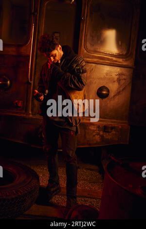 thoughtful man looking at spare part of rusty subway carriage in post-apocalyptic underground Stock Photo