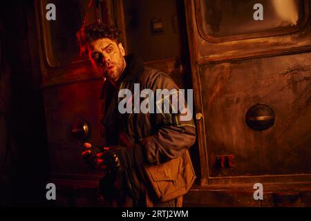 scared man looking away near abandoned subway carriage in red light, post-apocalypse concept Stock Photo