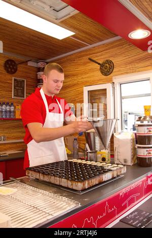 Man making poffertjes in a stall at the Albert Cuypmarkt in Amsterdam, Netherlands in spring. Man making poffertjes, typical small pancakes, at the Stock Photo