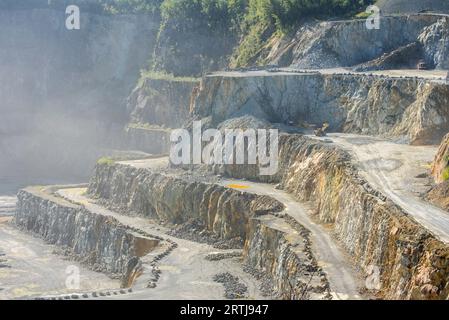 Heavy machines working in dusty porphyry quarry, open-pit mine for the production of gravel for road building at Lessen / Lessines, Hainaut, Belgium Stock Photo